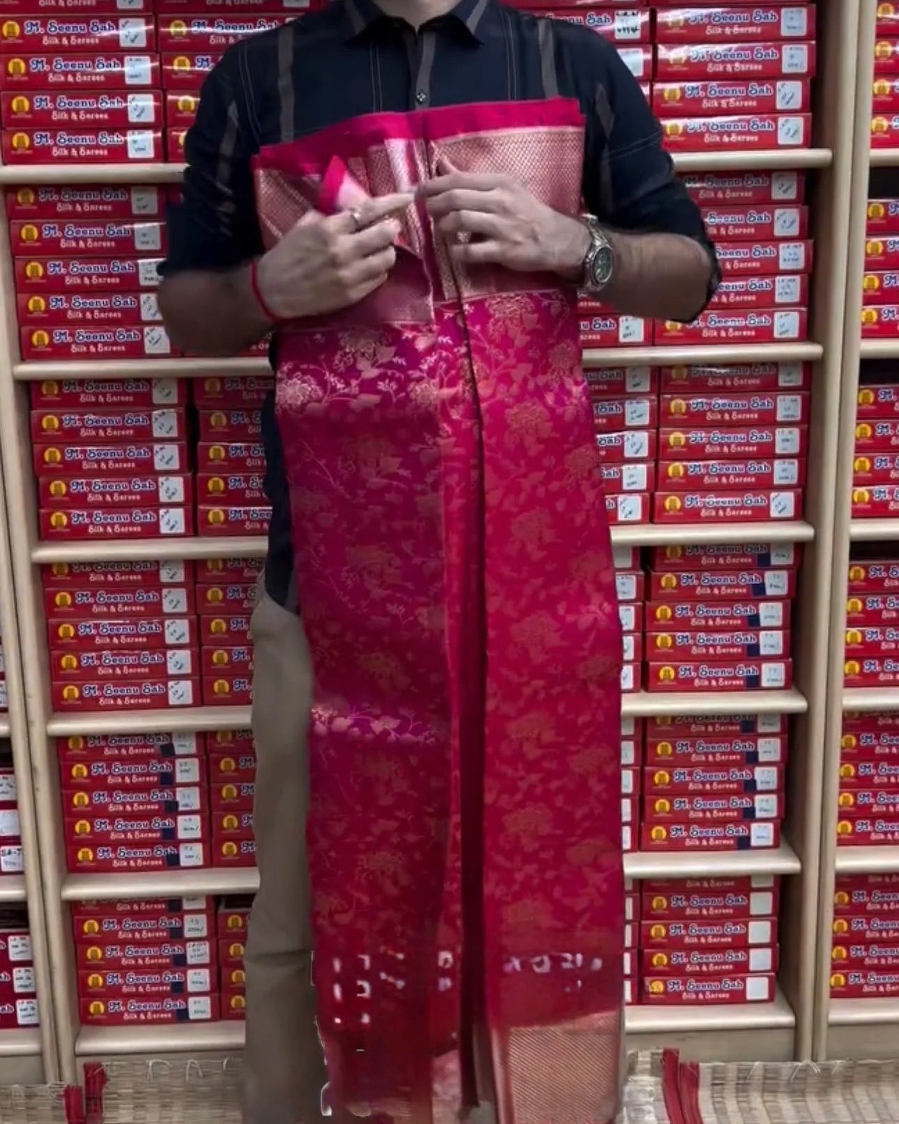 Person holding a red saree in front of shelves with red boxes.