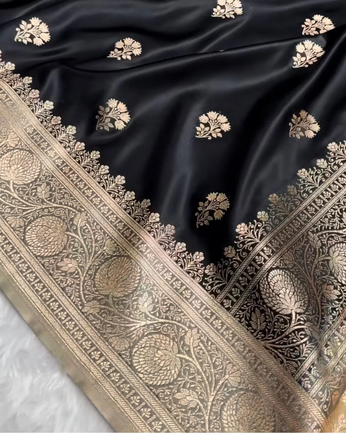 Black silk Banarasi fabric with gold zari floral motifs and an ornate gold border.