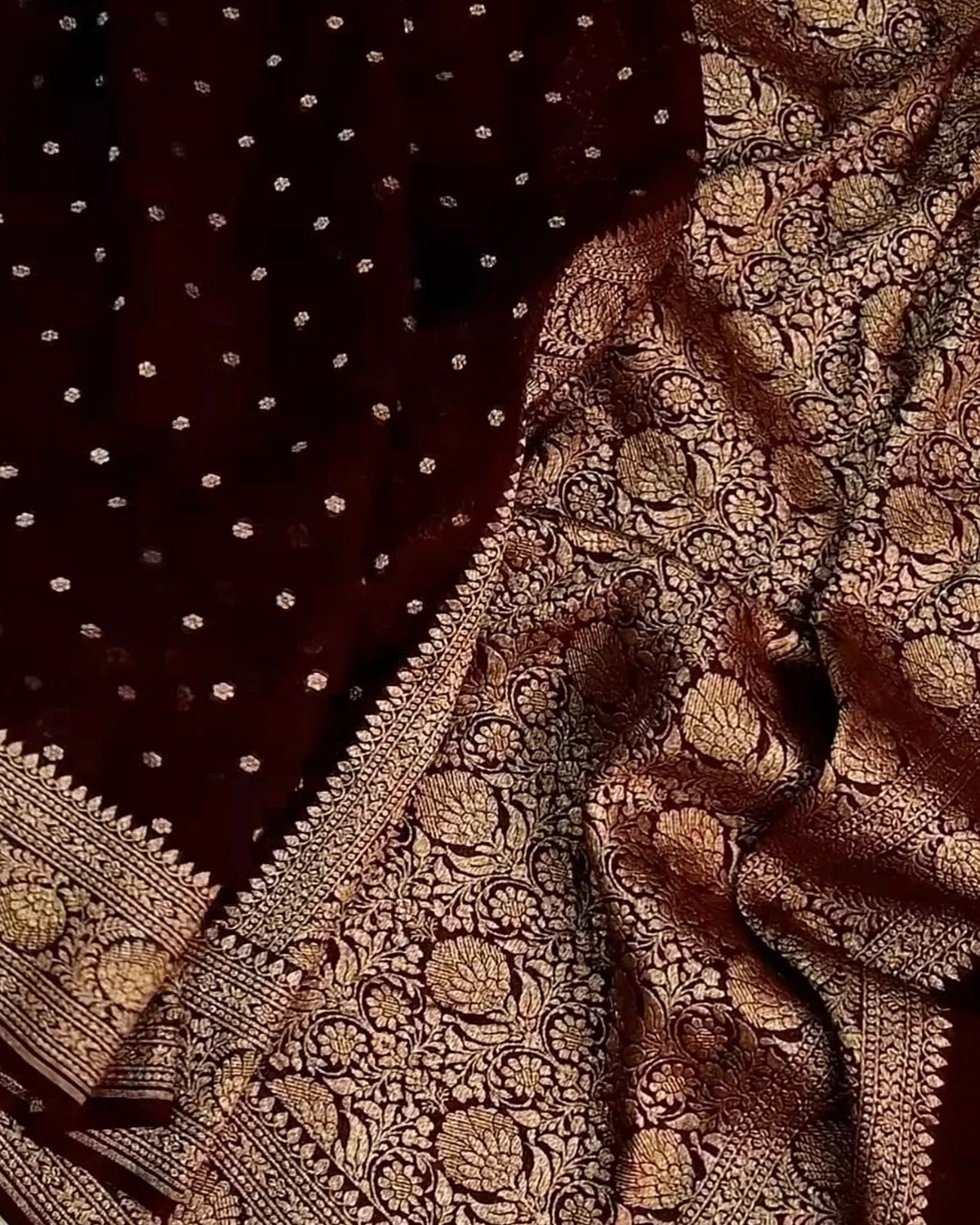 A close-up of a dark maroon or burgundy fabric with dense metallic gold woven floral patterns and small gold dots, likely a textile or scarf.