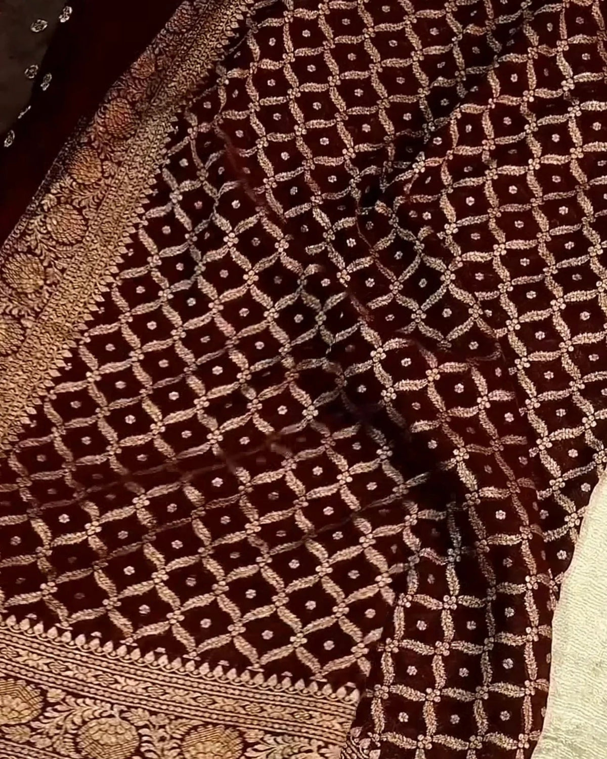 A close-up of a dark brown brocade fabric with an intricate gold geometric lattice pattern and a heavily embroidered border.