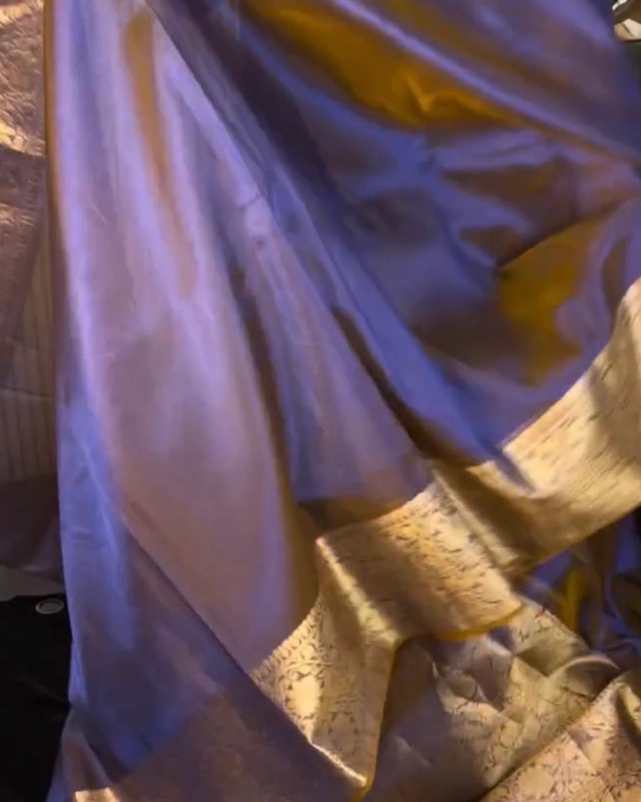 A draped purple and gold silk saree with a metallic zari border, shown in close-up folds.